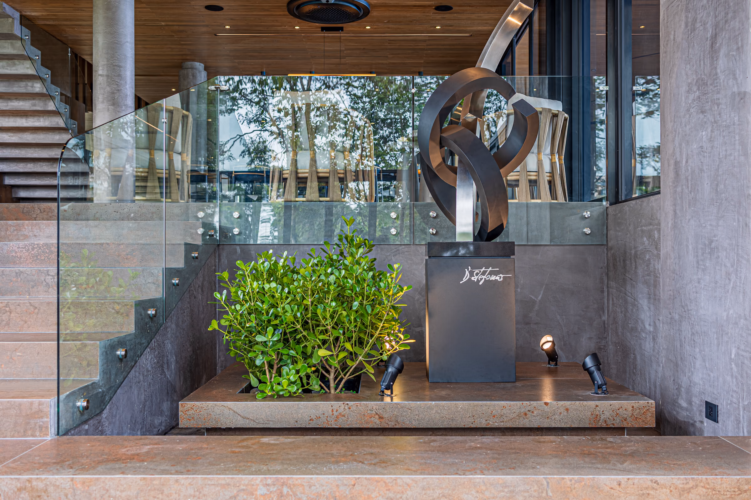 The entrance court: board-formed concrete walls, a planted bed and a sculptural bronze figure beside broad stone steps.