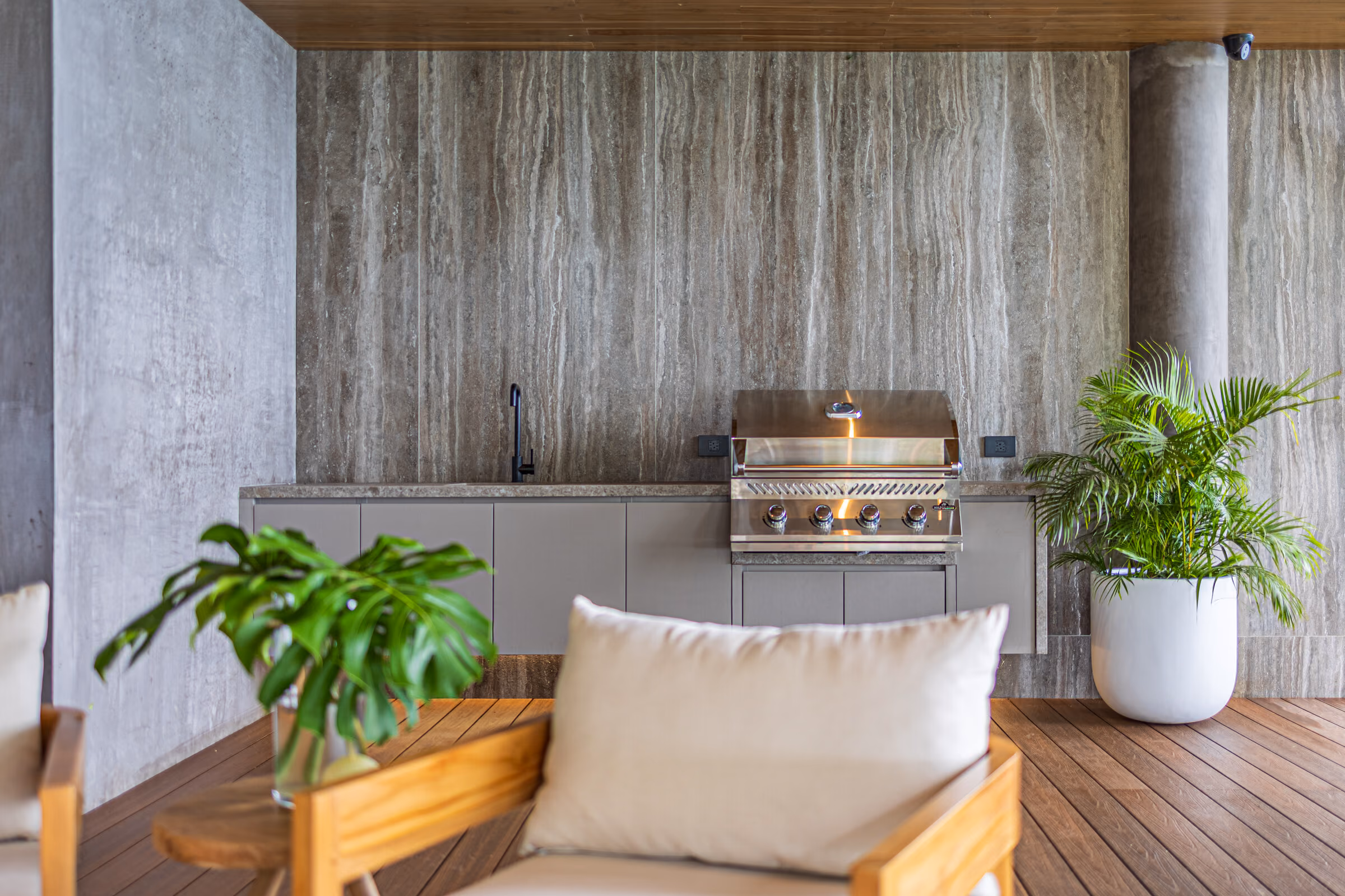 The barbecue terrace: a built-in grill in a stone counter, cushioned bench seating and planting, open to the pool deck.