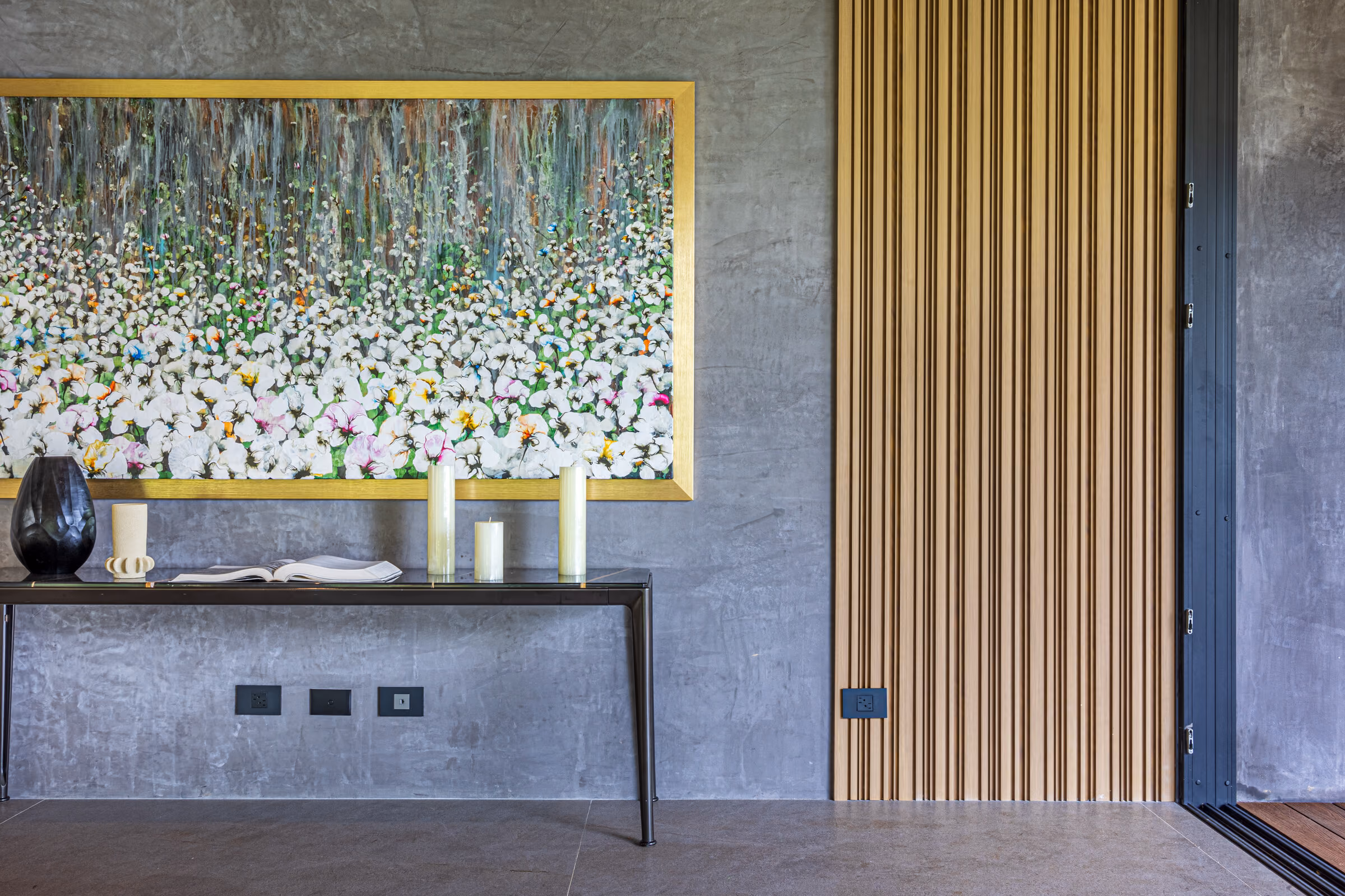 A console table against a fluted timber wall beneath a large textured painting.