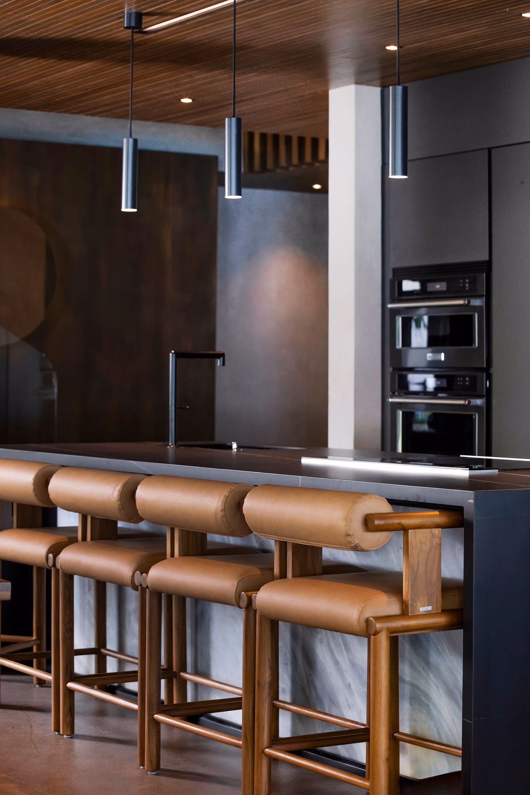 Close view of the tan leather bar stools at the stone-topped island, showing the stitched seat and slim timber frame.