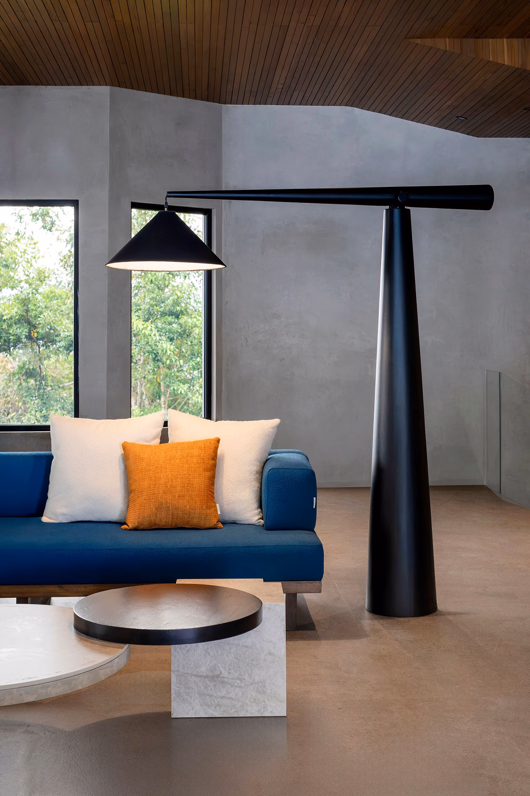 A cobalt blue sofa with a white and rust cushion beside a tall black sculptural floor lamp and a low round stone table.