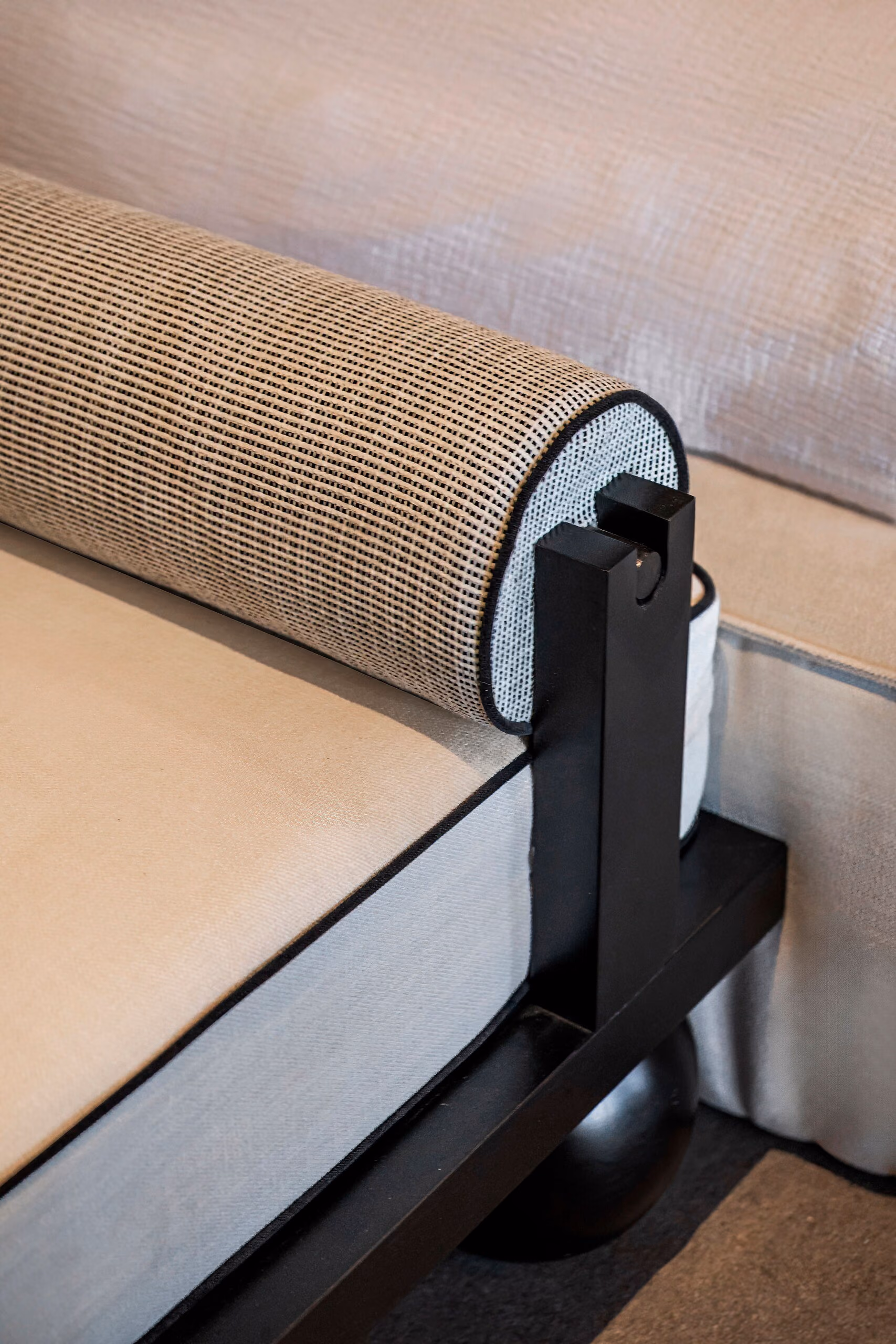 Detail of a woven bolster cushion held to a black metal frame by a leather strap and buckle.