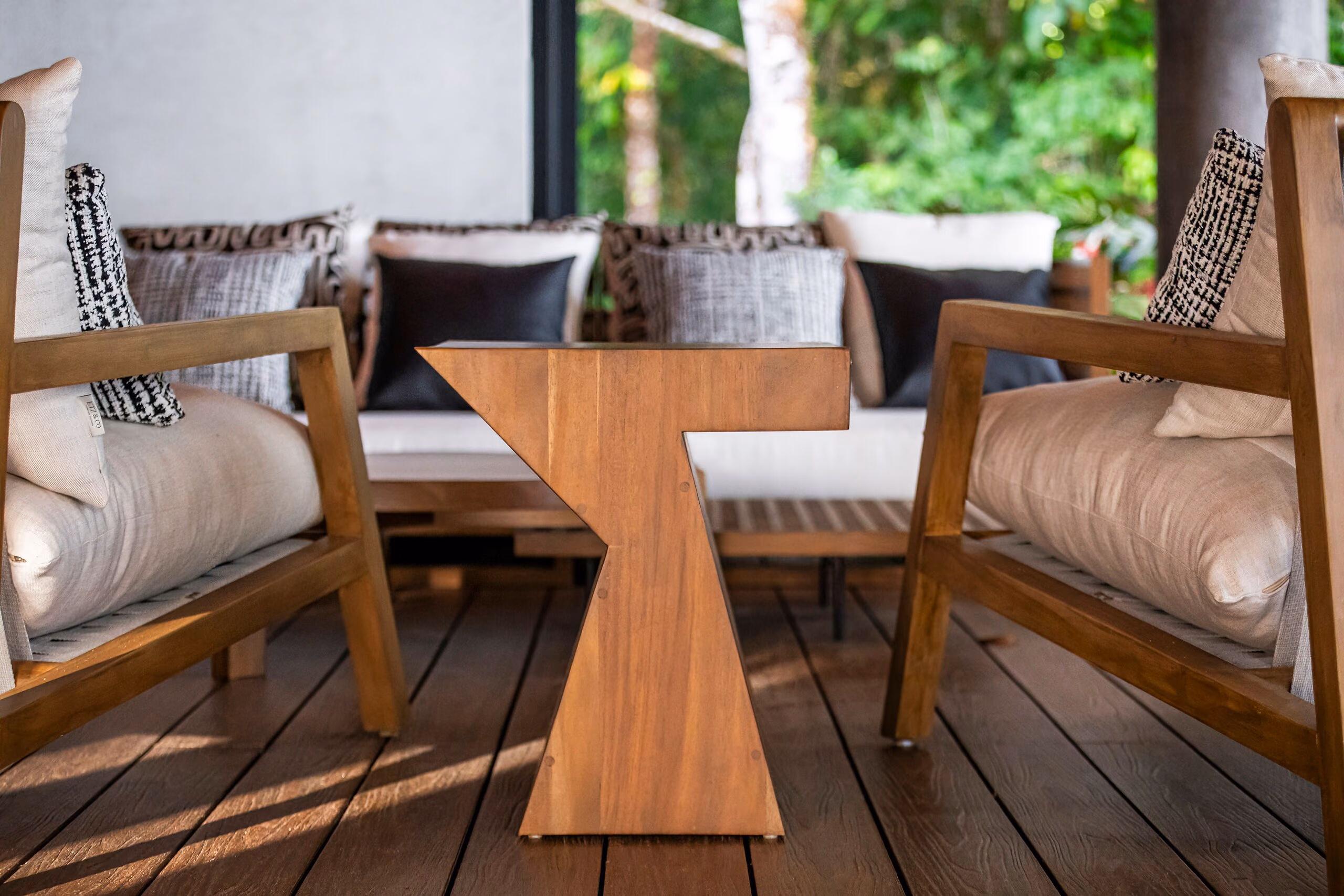 A terrace seating group of cushioned timber armchairs around a sculptural solid-timber table, open to the forest.