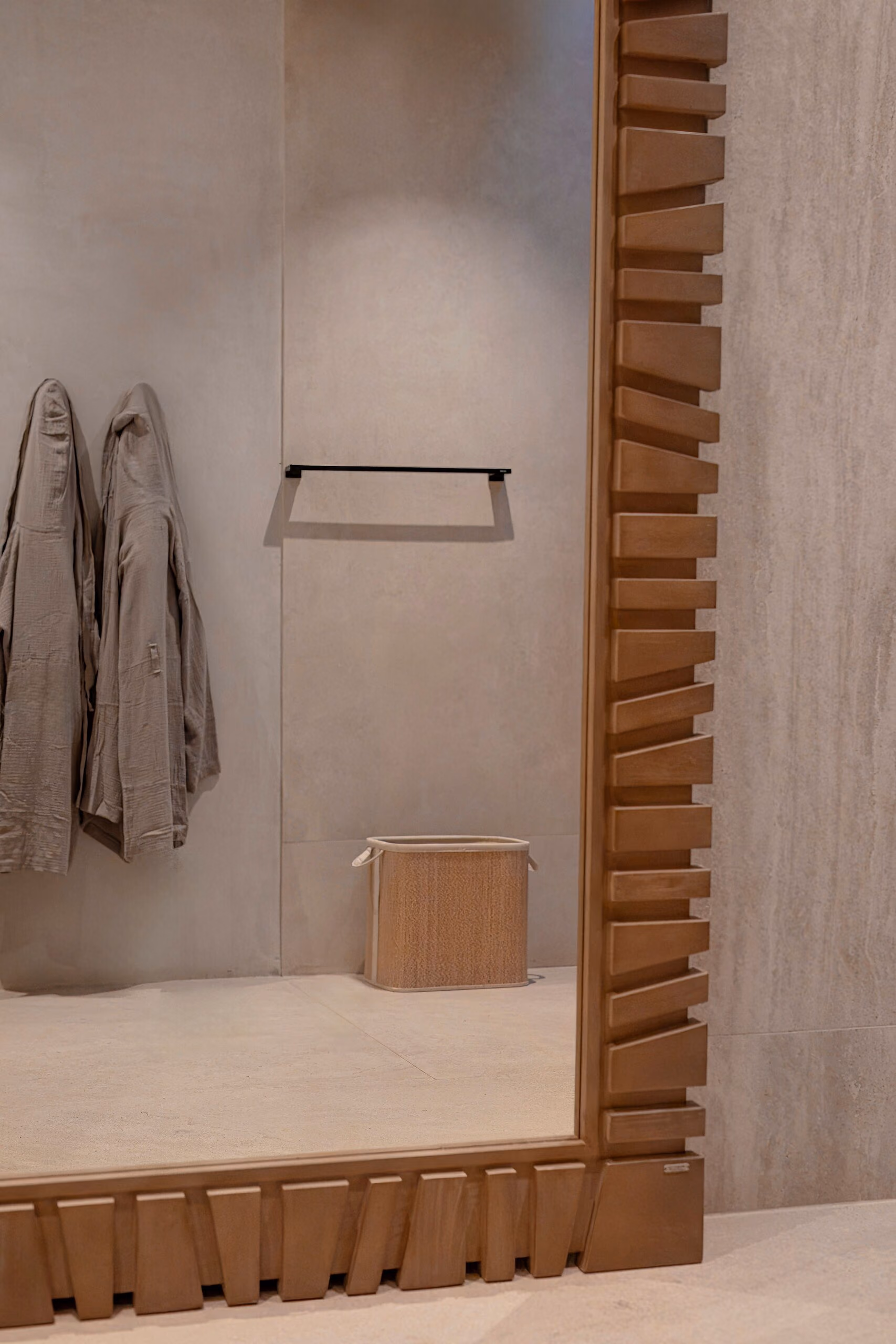 A full-height mirror in a fluted timber surround in the dressing area, with a rail and a woven basket alongside.