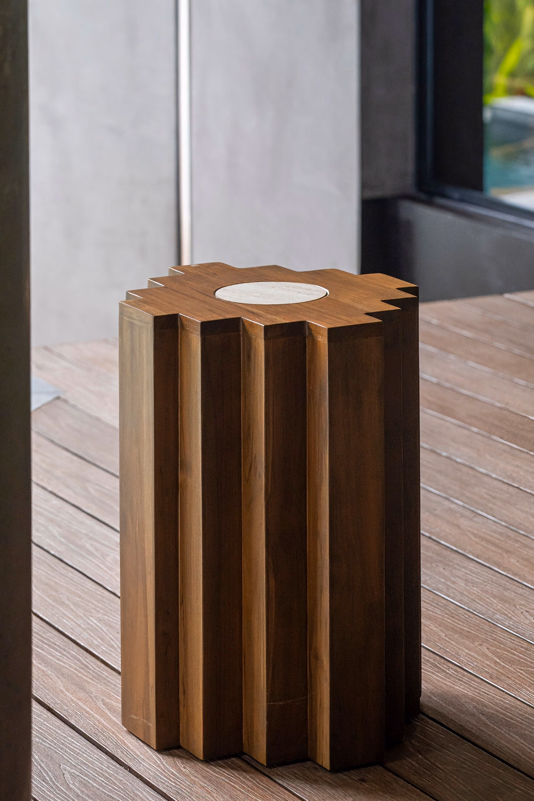 A fluted solid timber pedestal table with a pale inset top, standing on the terrace decking.