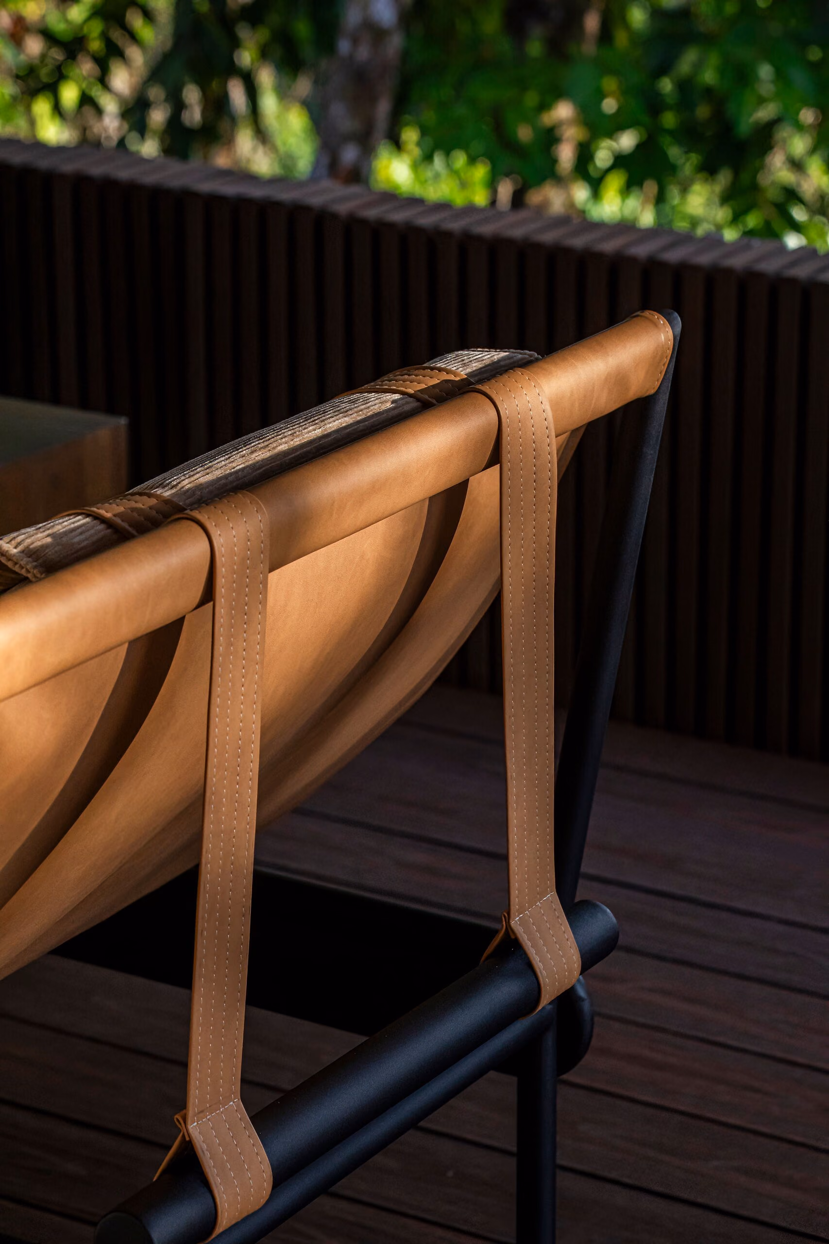 Detail of a chair where a tan leather seat is stretched and stitched over a bent timber and black metal frame.