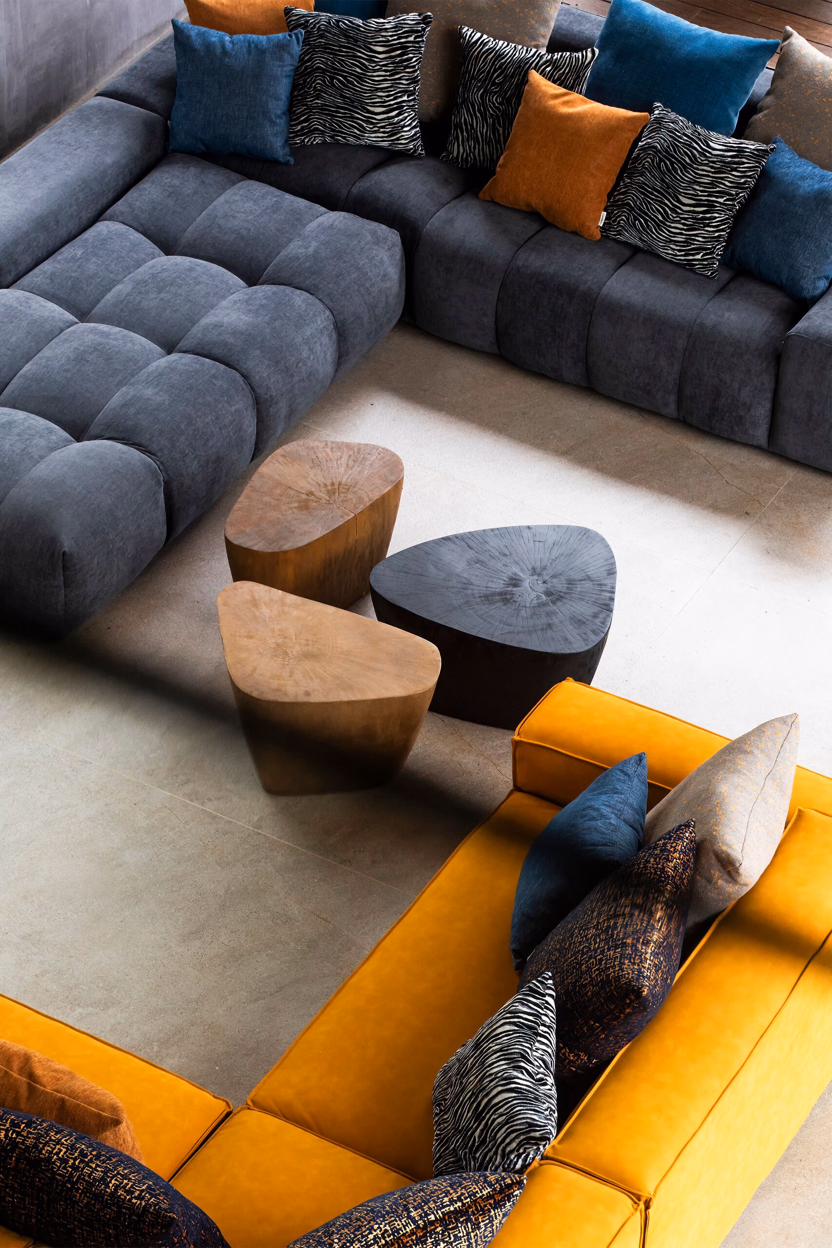 The sunken living room photographed from above, showing how the grey and ochre seating and the round timber tables are composed as one group.