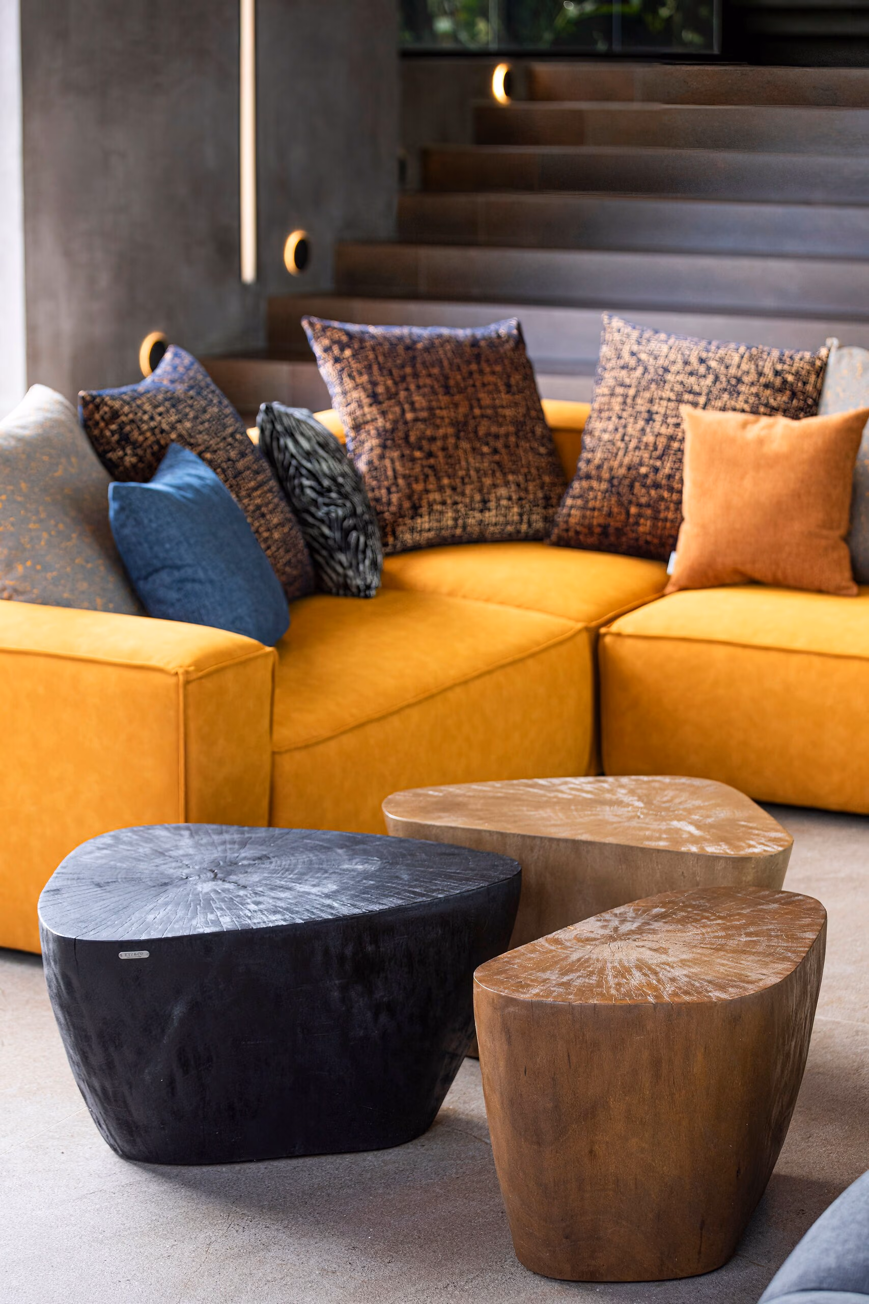 The ochre sofa in close view with a black stone side table and a solid timber stump table on a pale floor.