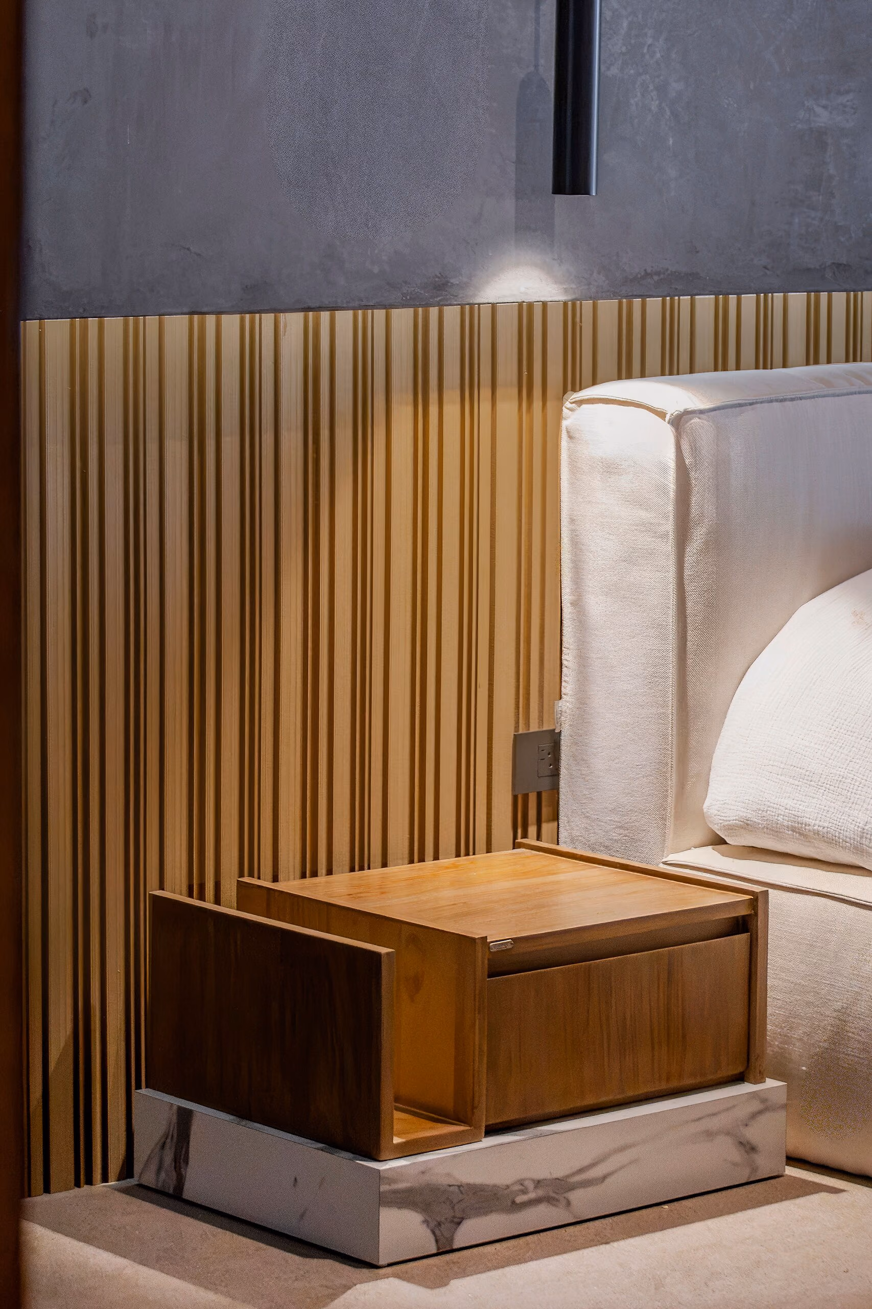 Detail of the open timber nightstand and the upholstered bed frame against the fluted brass wall.