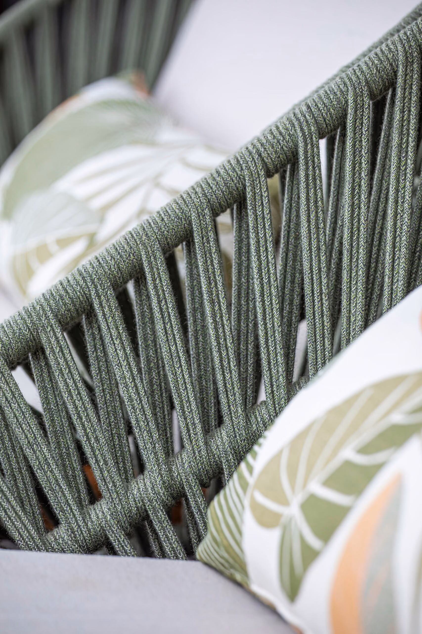 Close detail of the pale green woven rope back of an outdoor chair against a leaf-printed cushion.