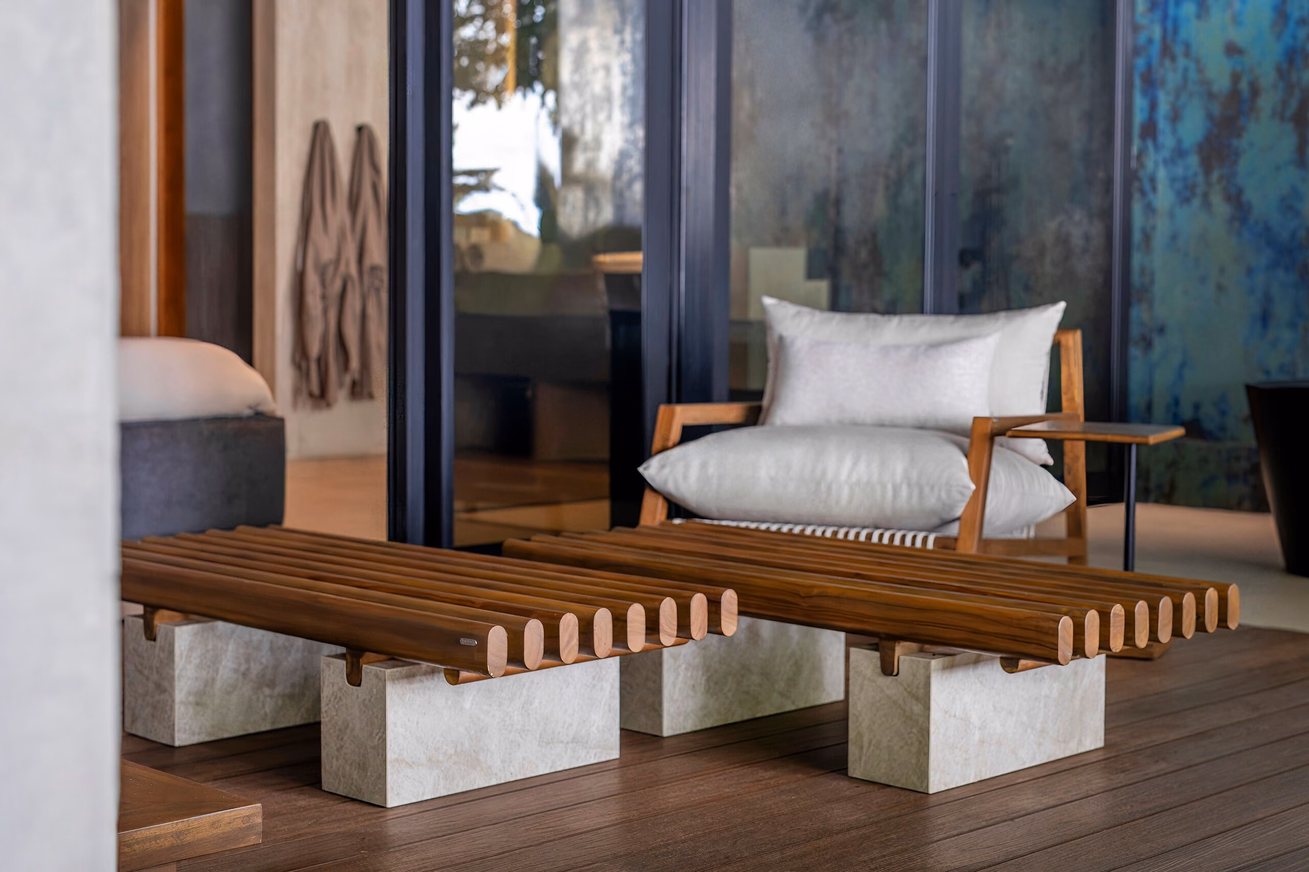 A long slatted teak bench resting on rough concrete blocks, set against a pale wall on the timber deck.