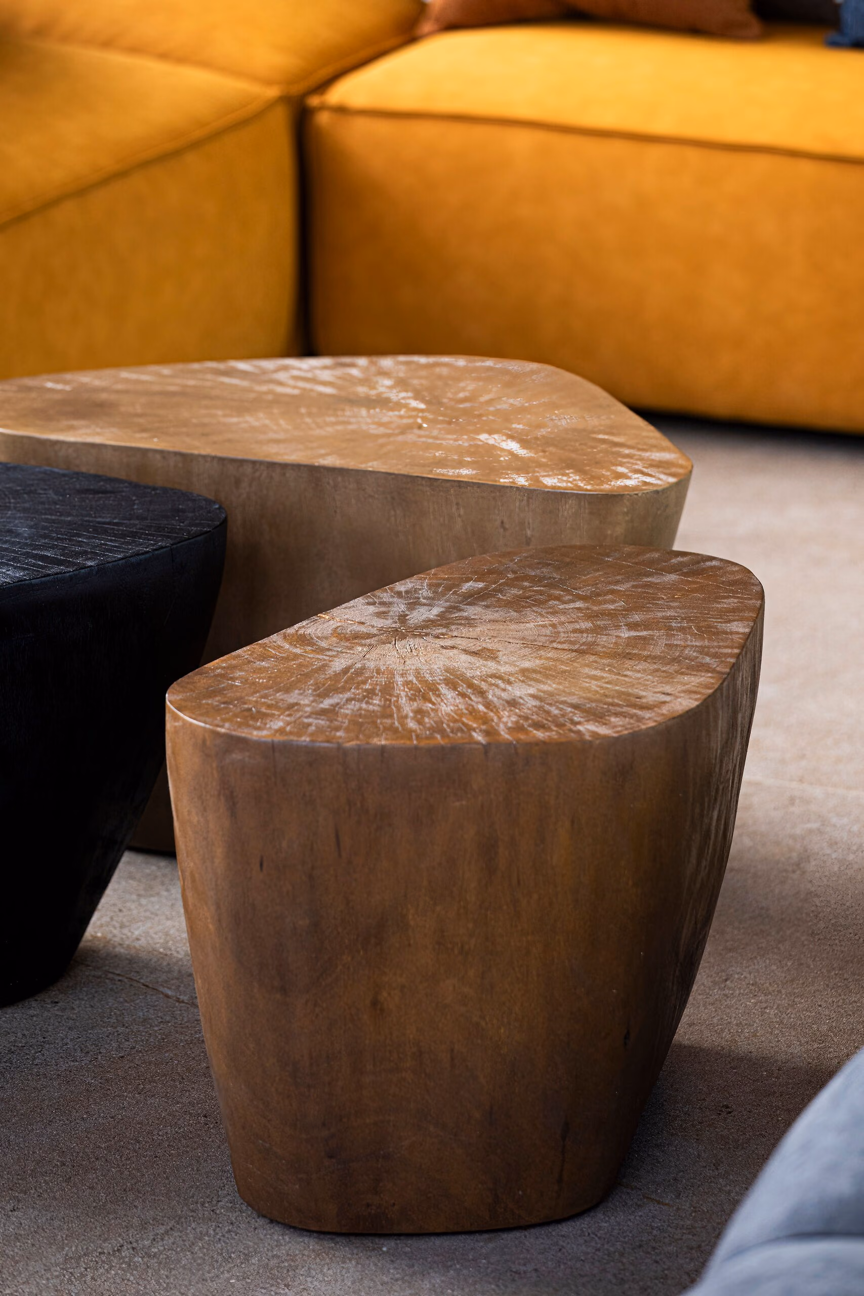 Two solid timber stump tables with visible end-grain, beside a black stone table and the ochre sofa.