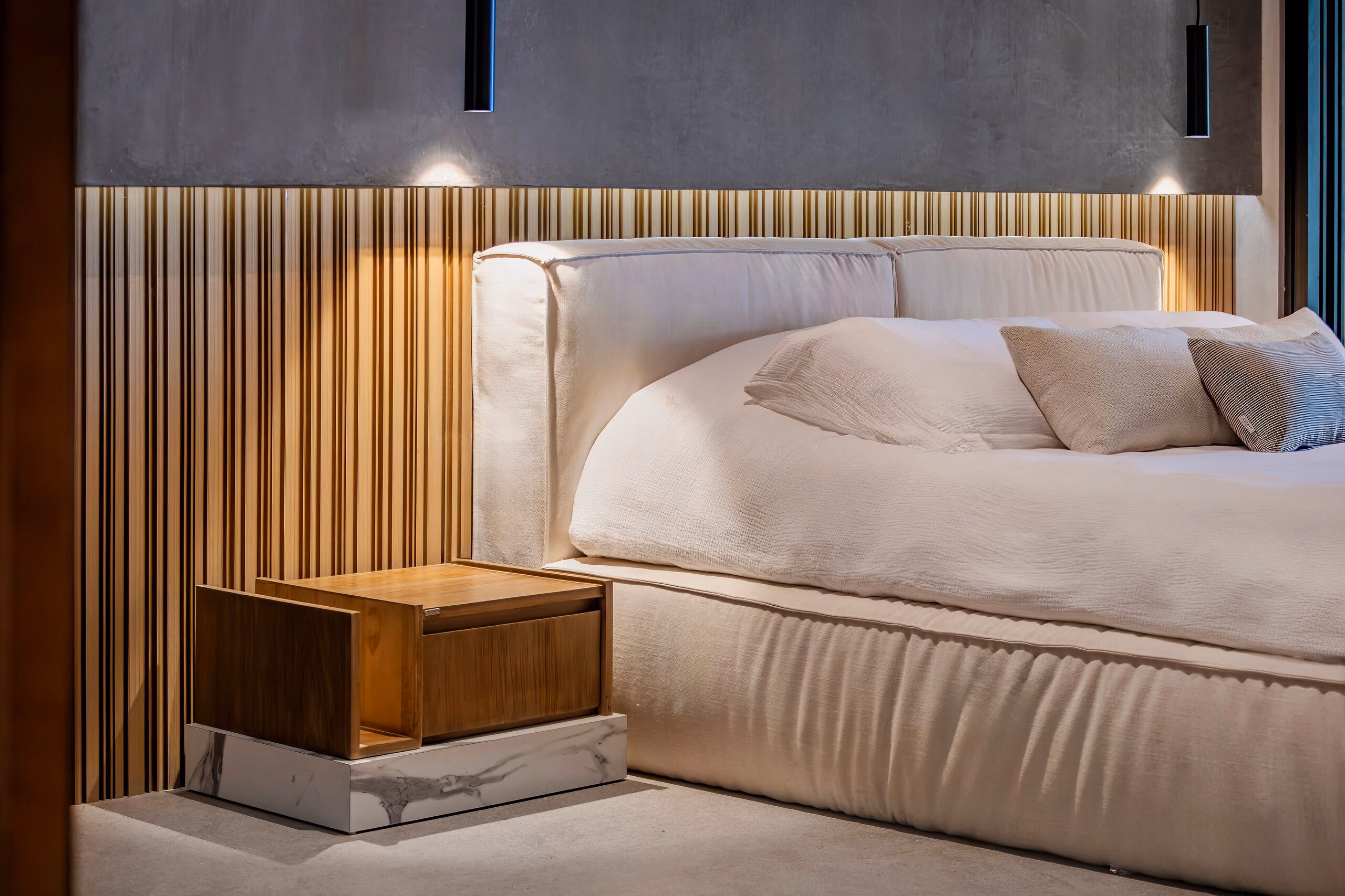 The principal bedroom: a low upholstered bed against a fluted brass headboard wall, with a timber nightstand alongside.