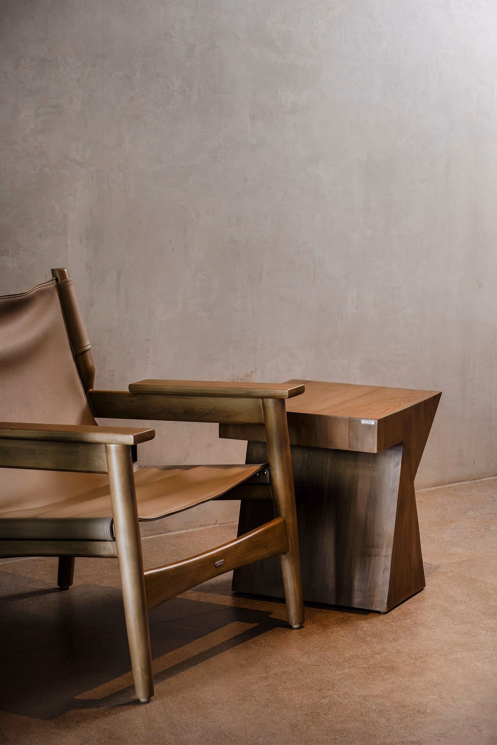 A leather sling chair and a carved timber side table in the corner of a bedroom, against a smooth plaster wall.