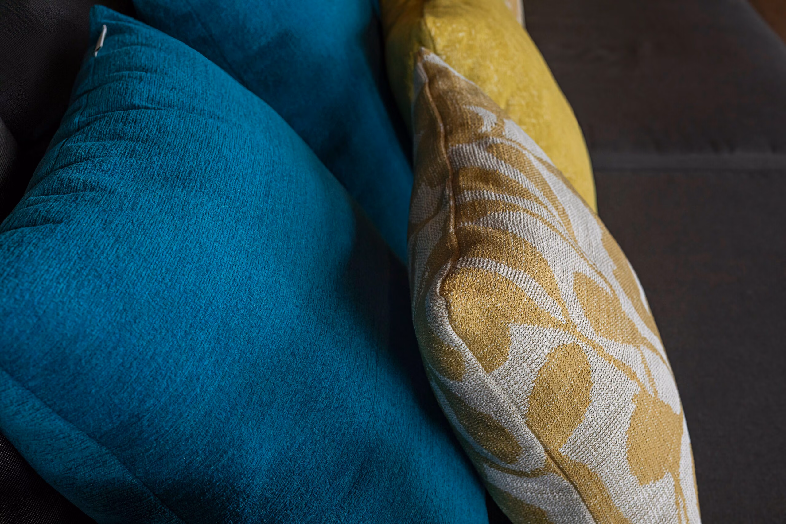 A deep teal bolster beside an ochre patterned cushion, photographed close in soft light.