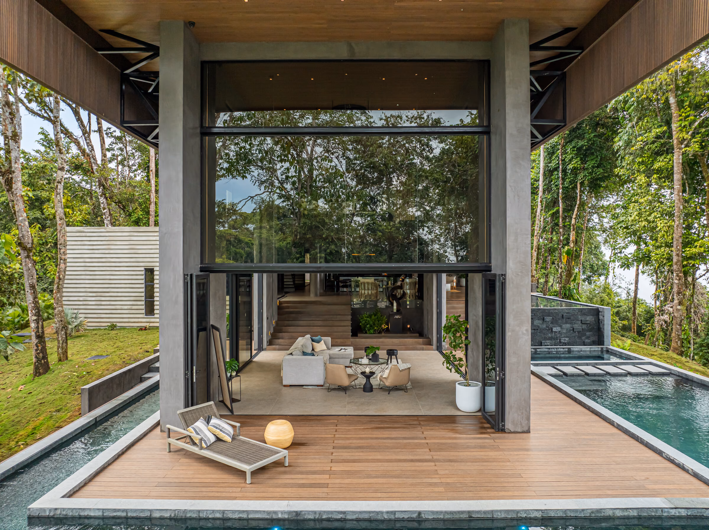 The lap pool running the length of the terrace, dark piers supporting the roof above, forest and ocean beyond.