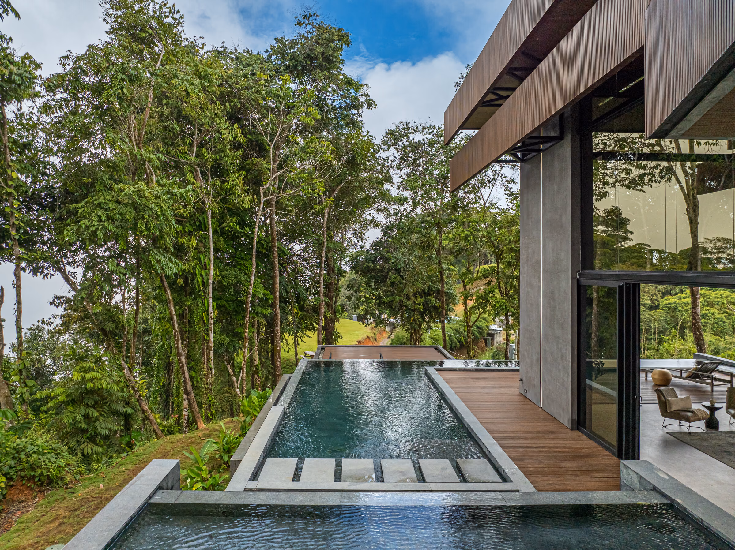 The residence along the axis of its lap pool, dark piers framing the forest.